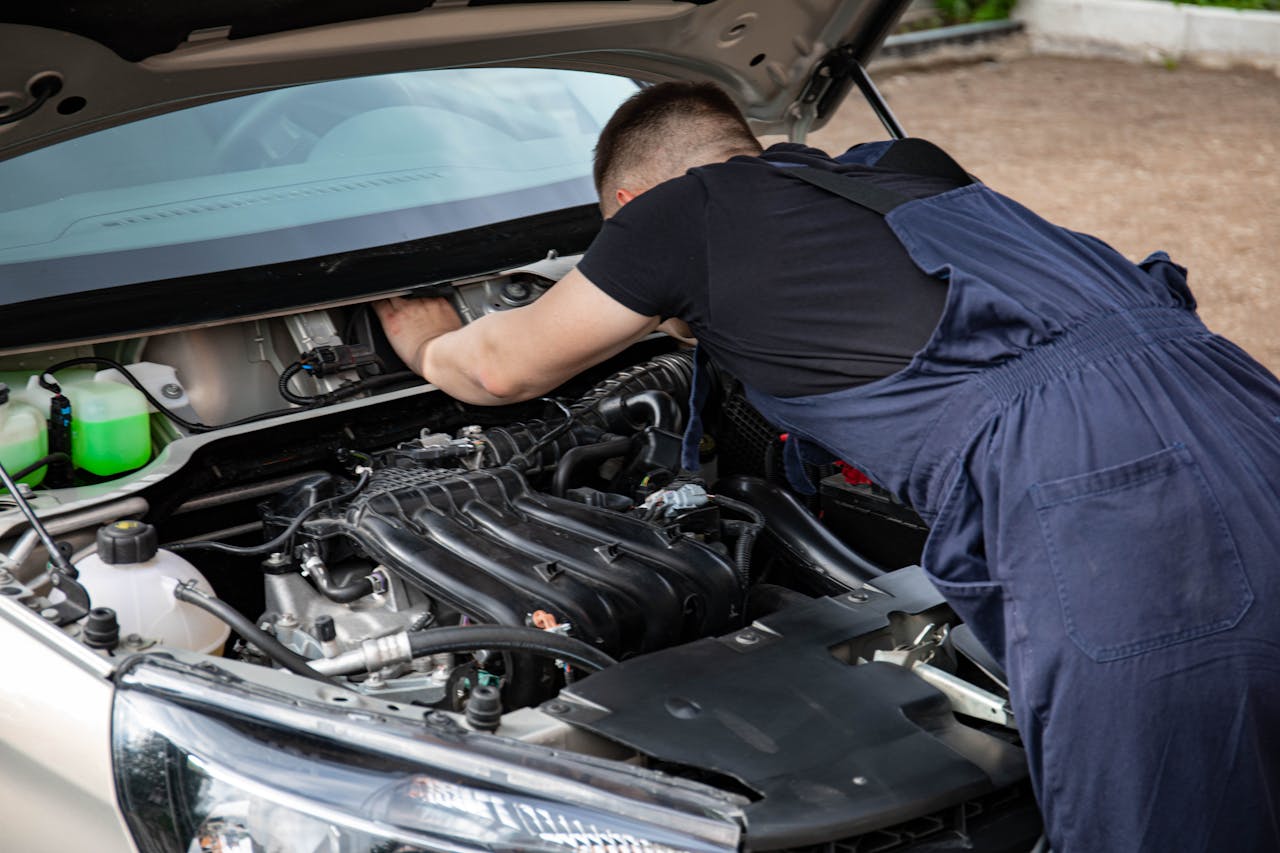 Mechanic working on car engine maintenance outdoors, showcasing skills and expertise.
